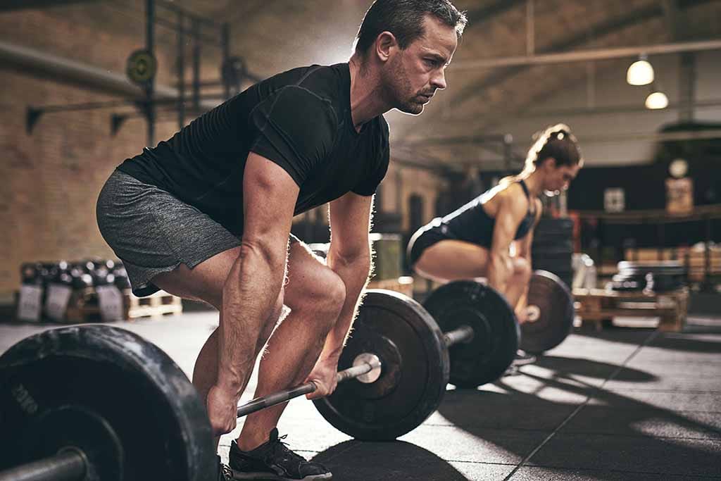 A man and a young girl doing barbell deadlift at gym.