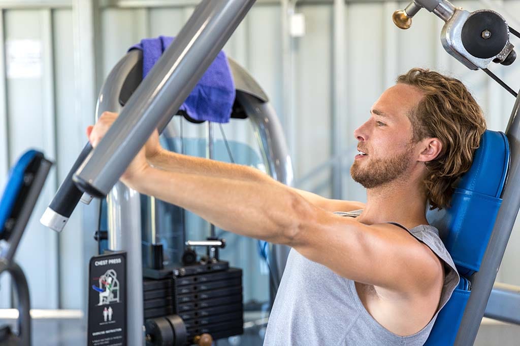 Man working with chest press machine at gym.