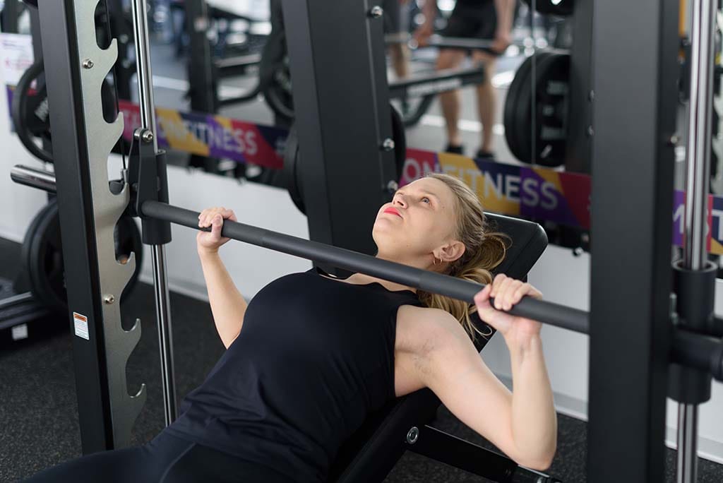 Woman lifting weights with Smith machine.