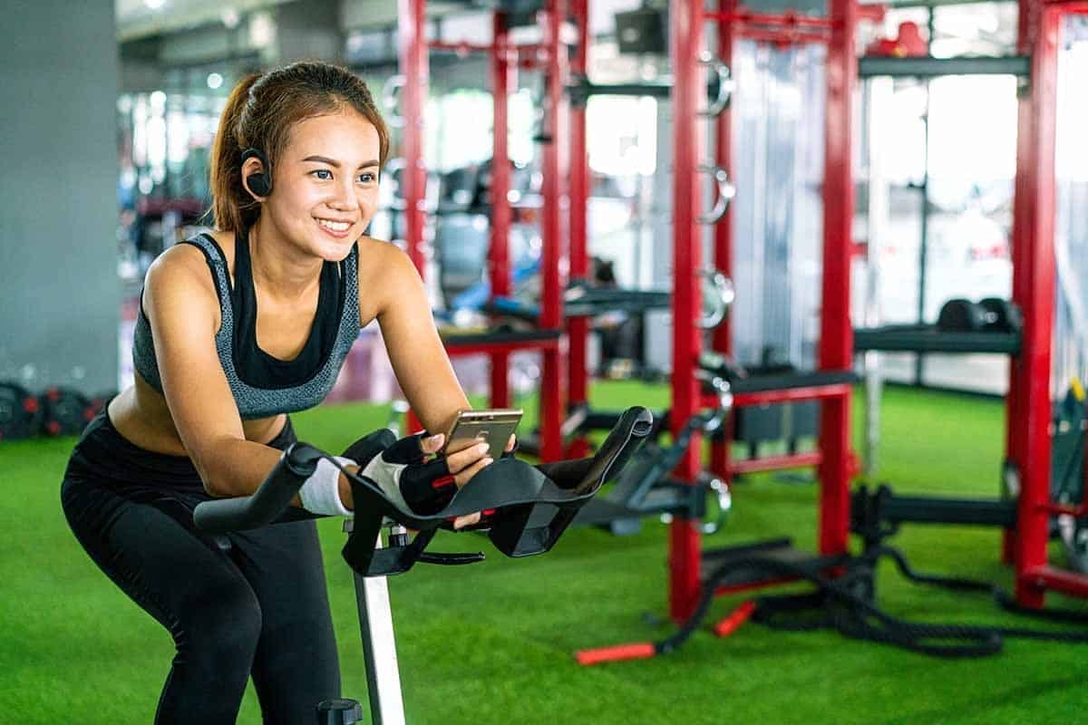 young woman doing leg workout on upright bike at gym