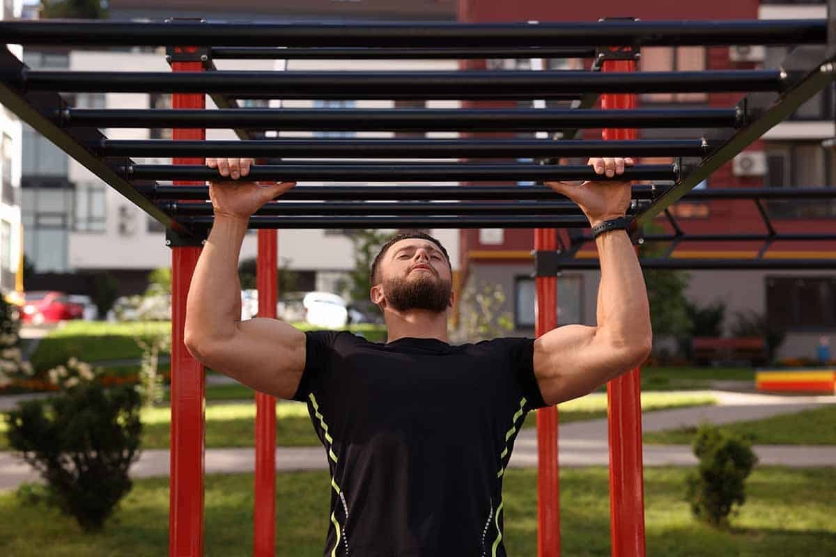 A man pulls himself up to the monkey bars. This is a good outdoor equipment substitute if you’re working on pull-up alternatives