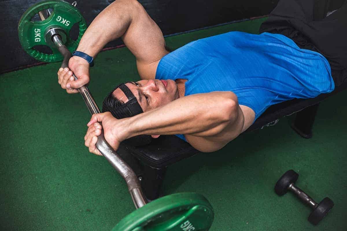 A man performs EZ bar skull crushers on a flat weight bench.