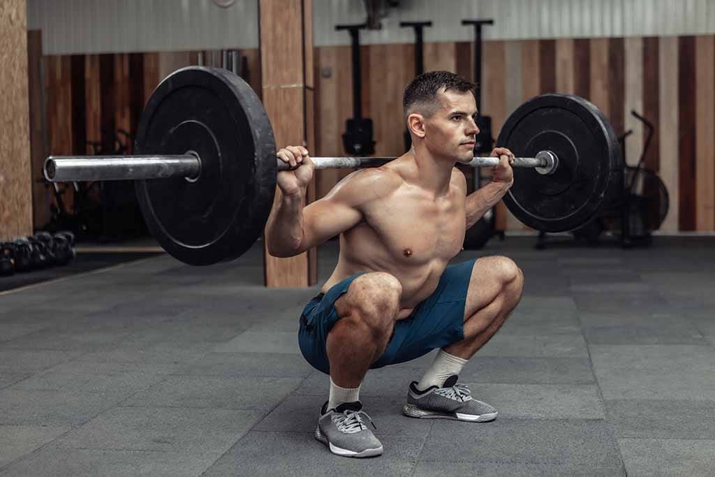 A man performs a high bar back squat with a barbell. 