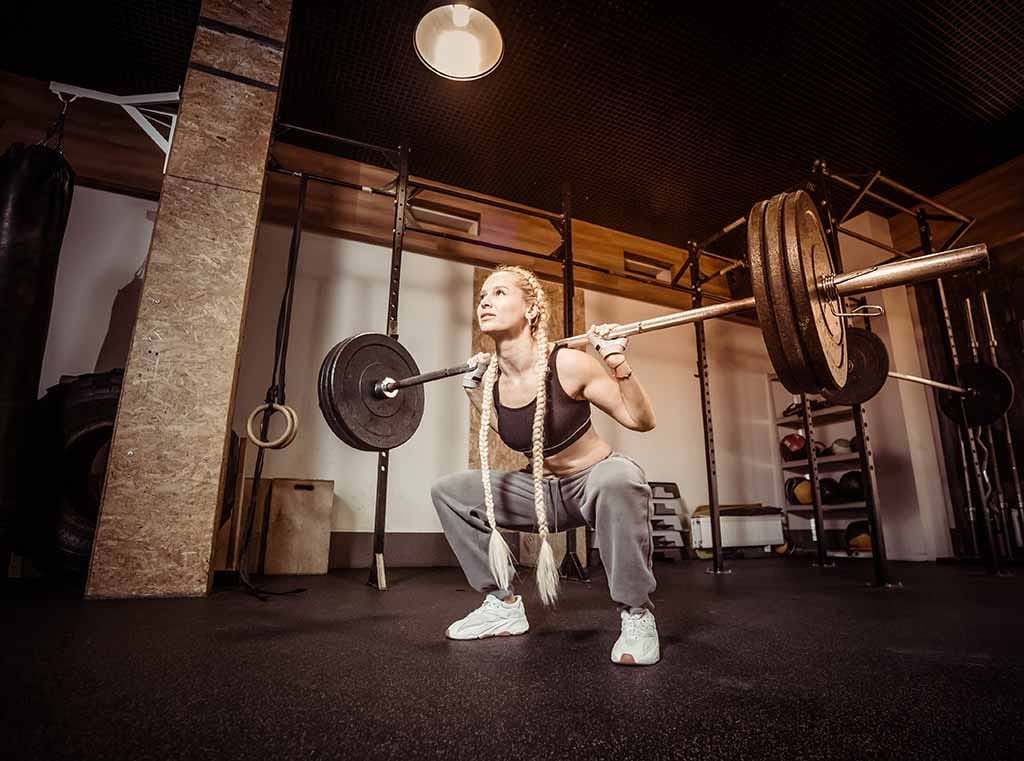 A woman does a barbell squat using a sumo stance.