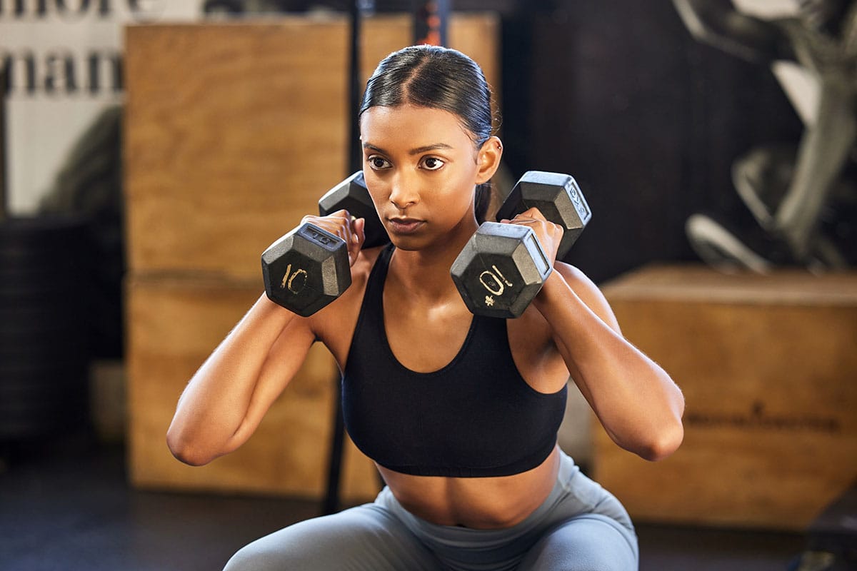 young girl doing dumbbell squats at gym