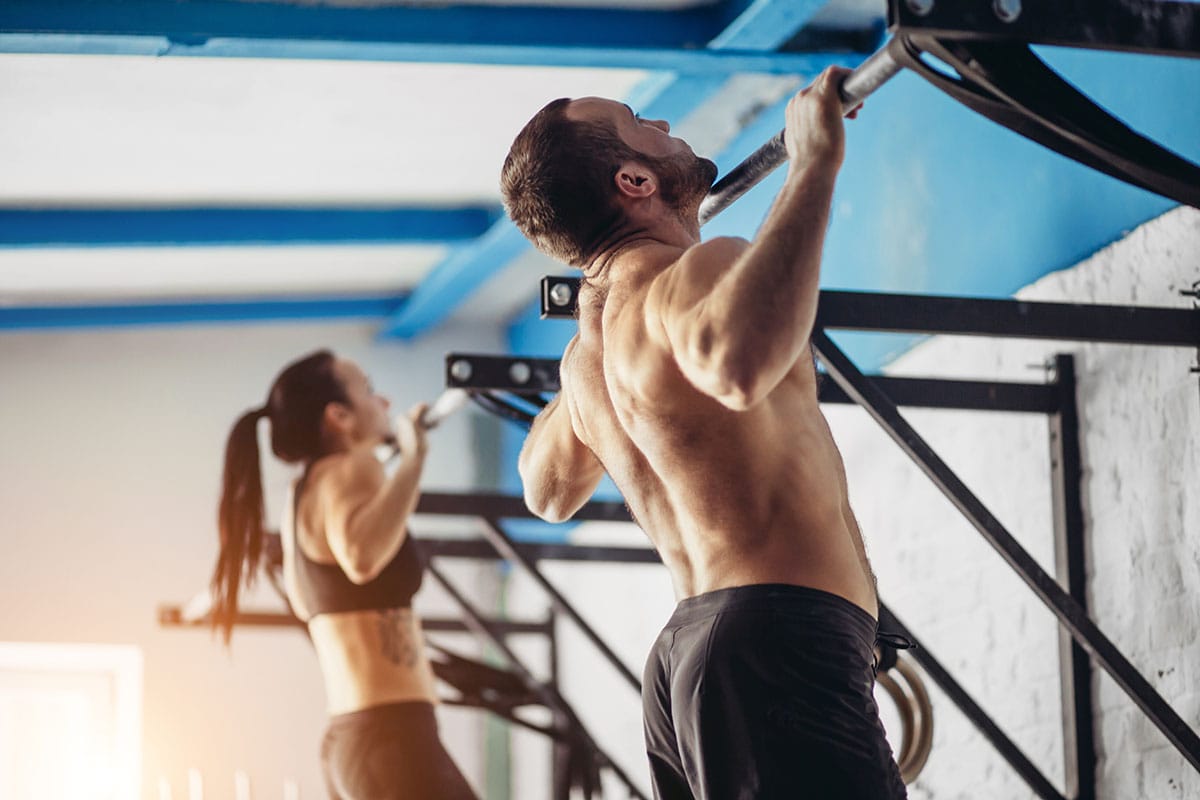 A man and a woman doing pull ups at gym