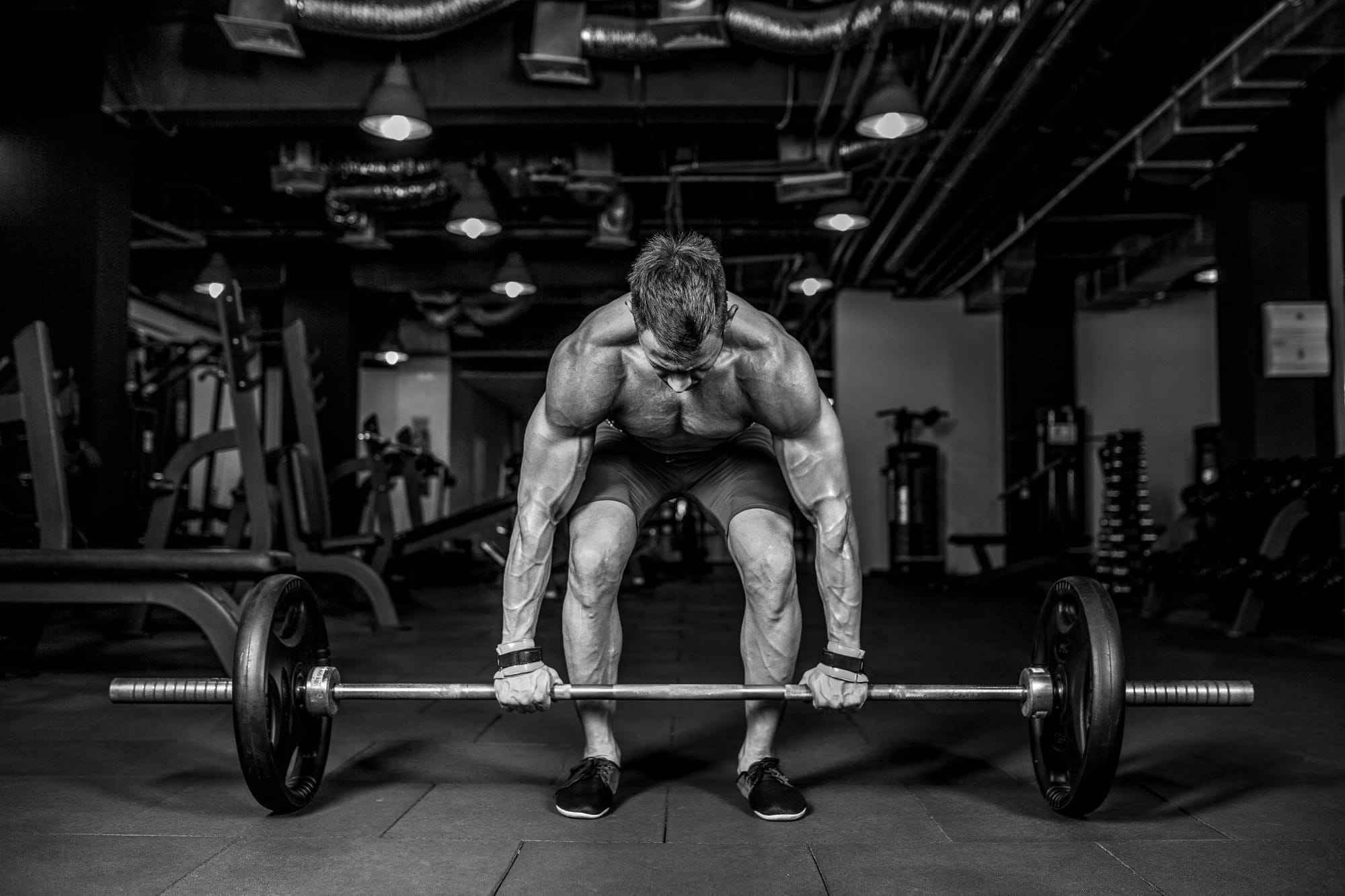 Black and white image of a muscular man preparing to deadlift in a gym