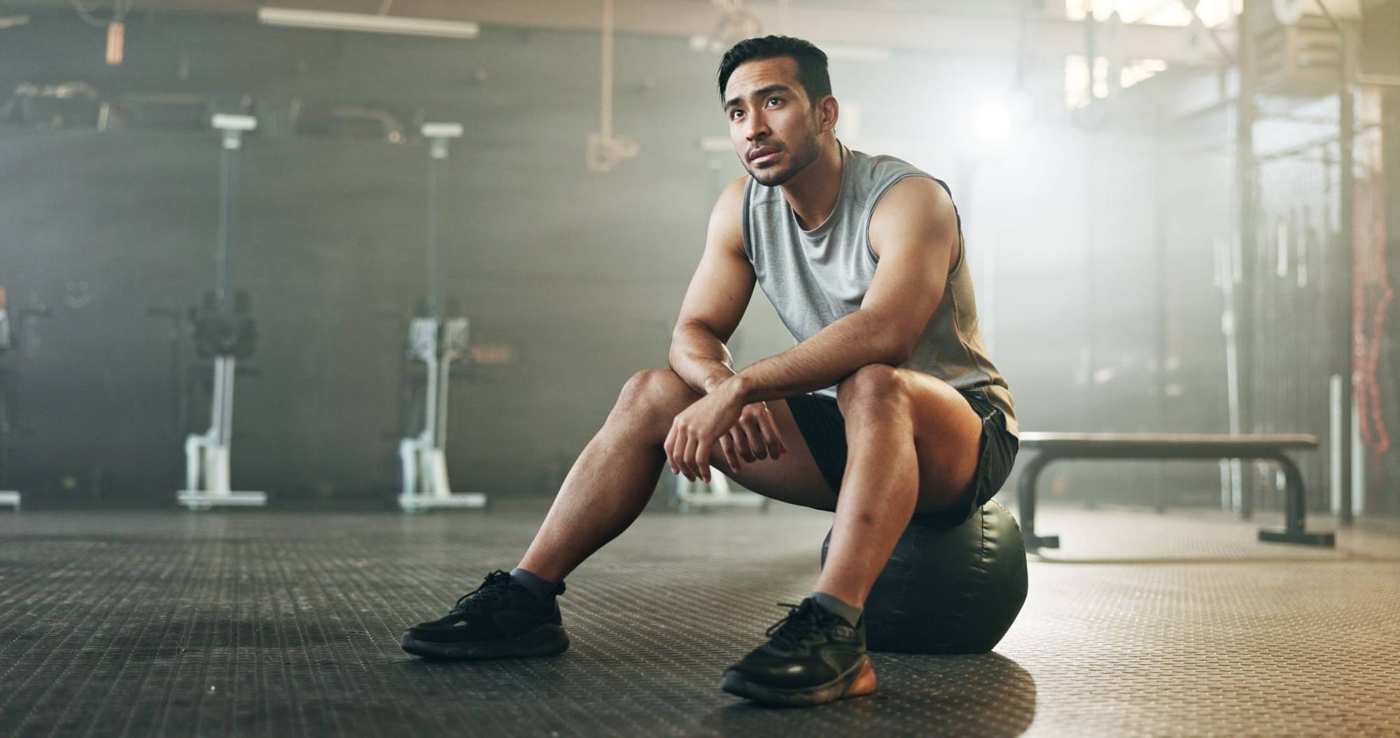 Athletic man sitting on a medicine ball in a gym, resting.