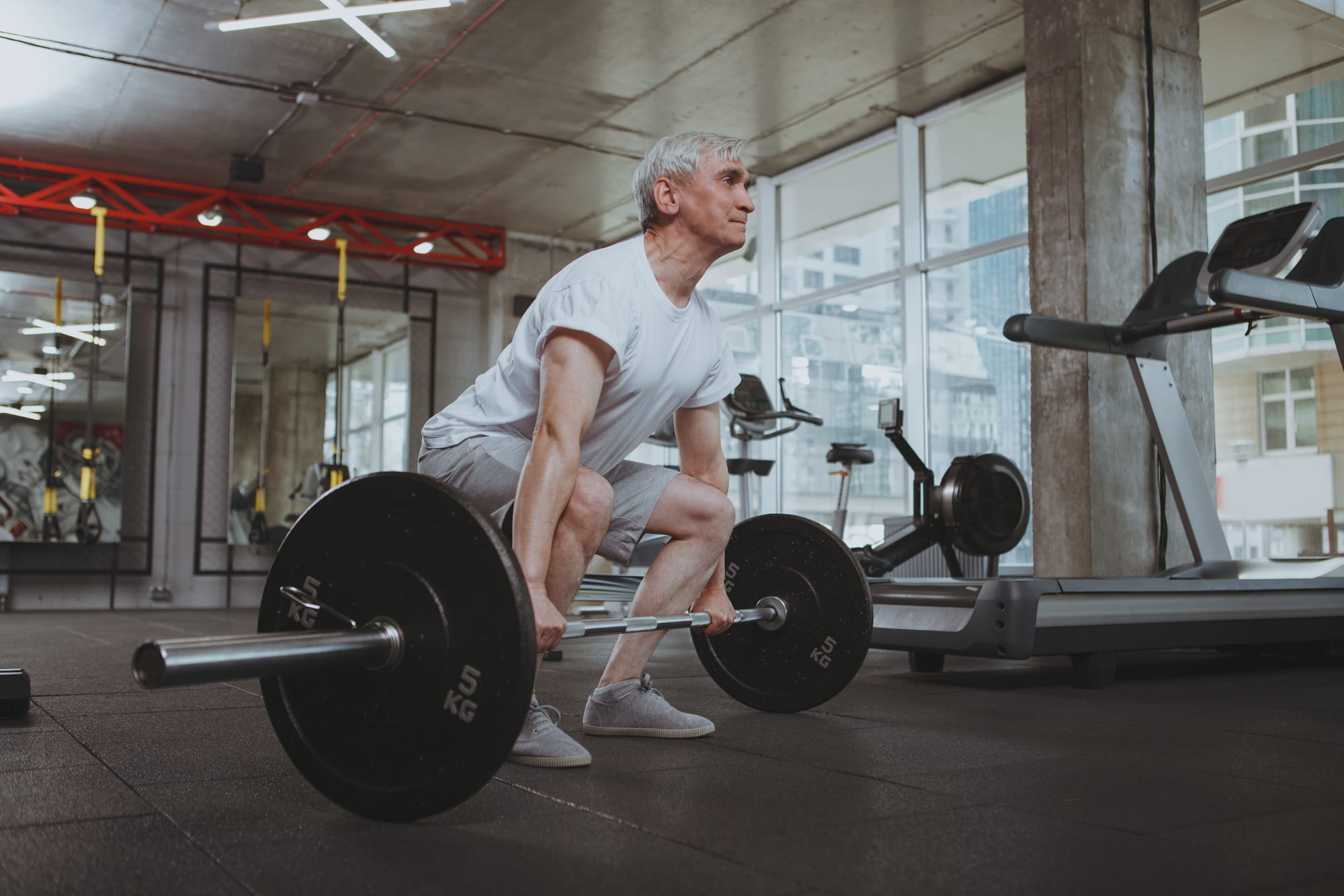 Senior man performing a deadlift in a modern gym, demonstrating strength training for longevity