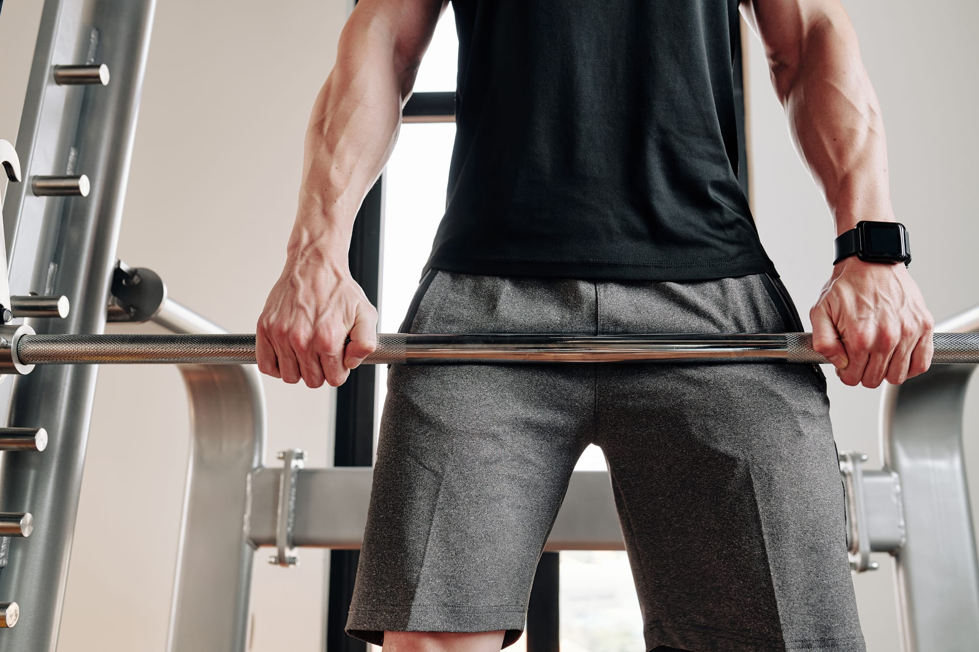 Close-up of a man's hands gripping a barbell in a gym, preparing for a Romanian Deadlift