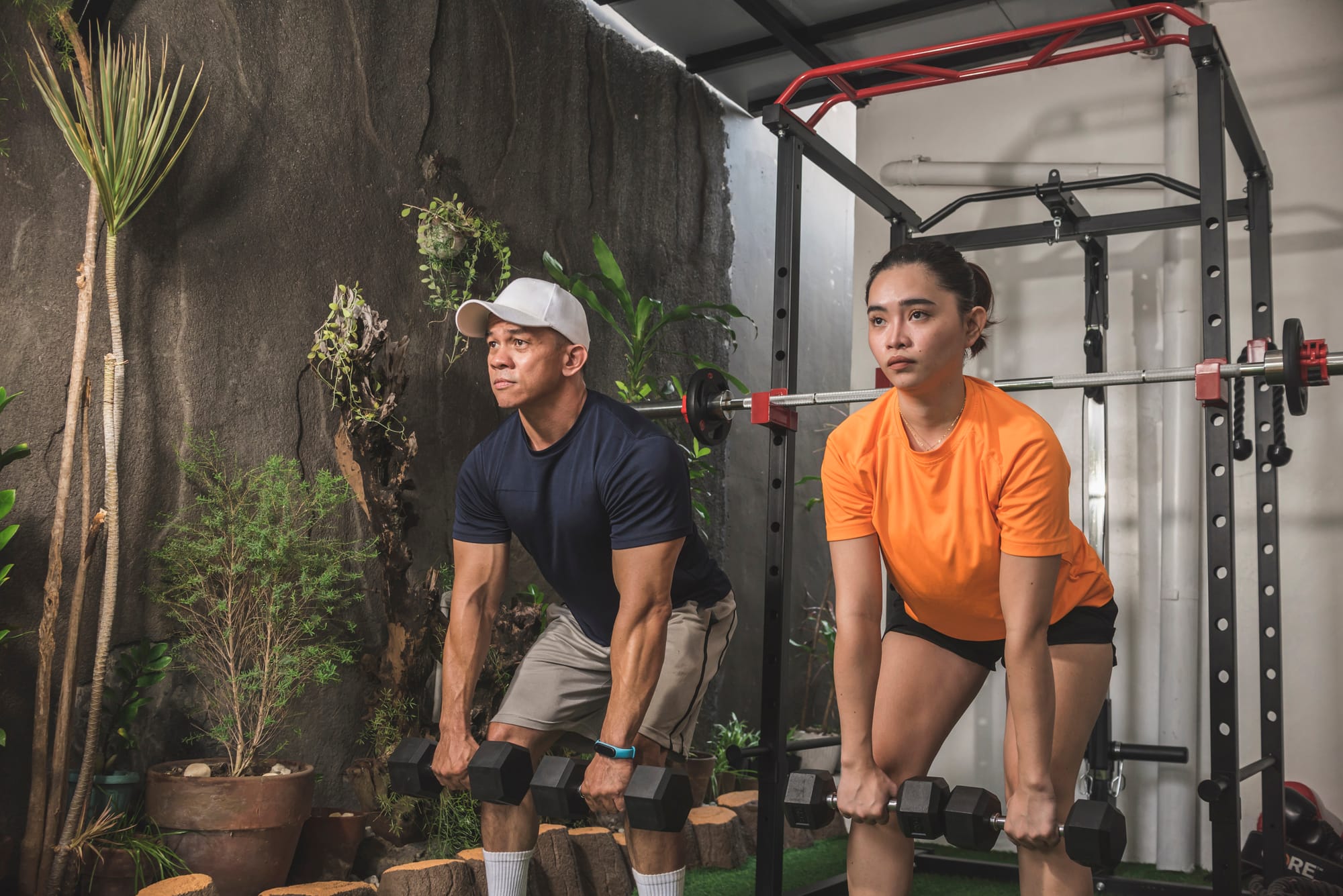  Man and woman performing Romanian deadlifts with dumbbells in a home gym.